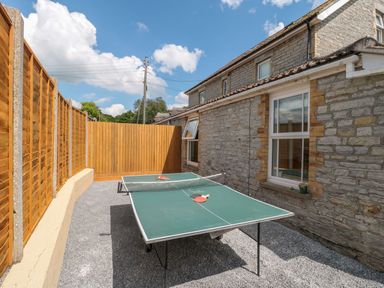 An outdoor area with a ping pong table between a stone house and a wooden fence at Metcalfe House in Compton Dundon
