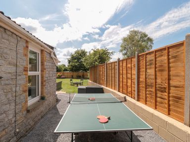 An outdoor area with a ping pong table alongside a stone house and a wooden fence at Metcalfe House in Compton Dundon