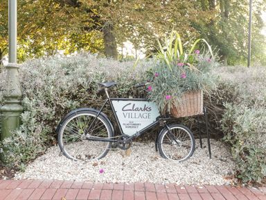 A black bicycle with a basket of plants in a garden area with a Clarks Village sign near Glastonbury Somerset