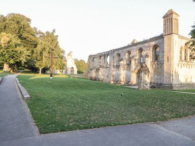 An outdoor scene with grassy area trees walking paths wooden cross and ruins of an old stone building at Metcalfe House in Compton Dundon