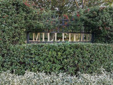 A metal sign with the word millfield surrounded by green hedges and red berries