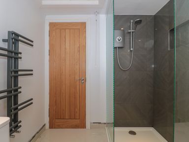 A bathroom with a wooden door a shower with dark tiles and a gray towel radiator at Metcalfe House in Compton Dundon