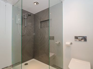 A shower area with glass panels and a wall-mounted showerhead next to a toilet with a toilet paper holder at Metcalfe House in Compton Dundon