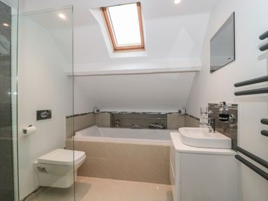 A bathroom with a bathtub under a skylight a wall-mounted toilet and a sink with a mirror at Metcalfe House in Compton Dundon