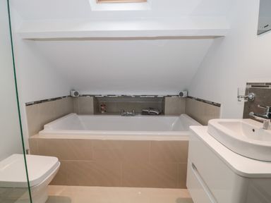 A bathroom with a bathtub under a sloped ceiling a toilet and a sink at Metcalfe House in Compton Dundon