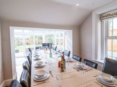 A dining room with a long table set with plates glasses and bottles of wine near a window at Metcalfe House in Compton Dundon