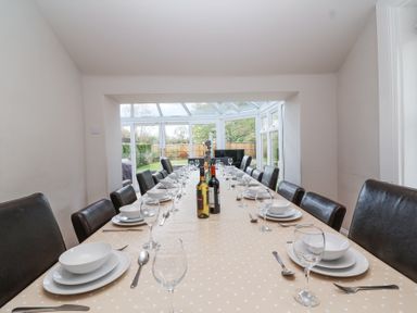 A long dining table set with plates bowls glasses and cutlery in a room with a glass extension at Metcalfe House in Compton Dundon