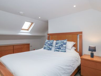 A bedroom with a bed with blue pillows a wooden dresser a nightstand with a lamp and a skylight window at Metcalfe House in Compton Dundon