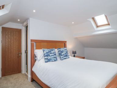 A bedroom with a wooden bed with white bedding and blue pillows skylight window and wooden door at Metcalfe House in Compton Dundon