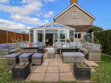 An outdoor patio with rattan furniture and cushions in front of a conservatory at Metcalfe House in Compton Dundon