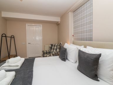 A bedroom with a bed with pillows towels an armchair a door and a window with a checkered blind at Metcalfe House in Compton Dundon