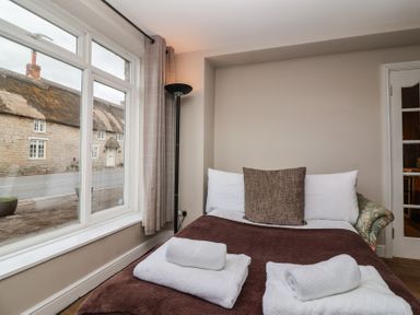 A bedroom with a bed covered with a brown blanket and white towels next to a window with curtains at Metcalfe House in Compton Dundon
