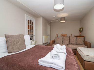A living room with a sofa bed with pillows and folded towels on it a brown couch a dining table with chairs and a wooden cabinet with flowers at Metcalfe House in Compton Dundon