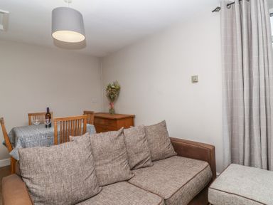 A living area with a brown sofa and cushions a wooden dining table with chairs and a sideboard with flowers at Metcalfe House in Compton Dundon