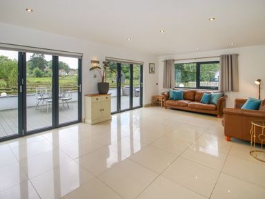 A living room with brown leather sofas blue cushions sliding glass doors and a small cabinet at Timberdyne Brimfield near Woofferton