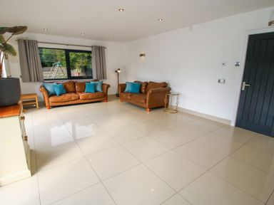 A living room with two brown leather sofas with blue cushions a floor lamp a small round side table and a large window with curtains at Timberdyne in Brimfield near Woofferton