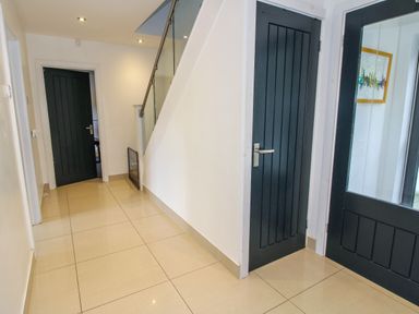 A hallway with beige tiled flooring black doors and a staircase with glass railing at Timberdyne in Brimfield near Woofferton