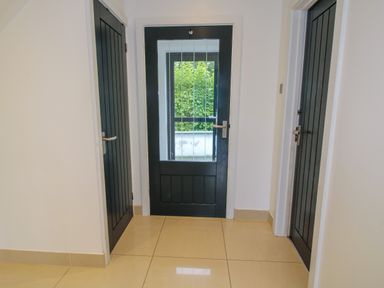A hallway with three black doors and beige tiled floor at Timberdyne in Brimfield near Woofferton