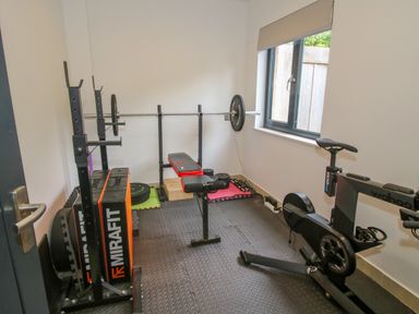 A home gym with weightlifting bench and barbell and an exercise bike near a window at Timberdyne in Brimfield near Woofferton