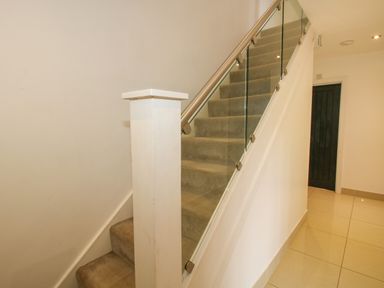 A carpeted staircase with glass panel railing next to a hallway with tiled floor and a dark door at Timberdyne in Brimfield near Woofferton