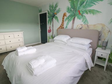 A bedroom with a large bed with white linens and towels a white dresser and a wall mural with animals at Timberdyne in Brimfield near Woofferton