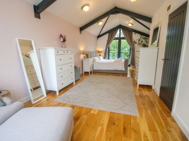 A bedroom with a bed lamps dressers mirror armchair and a rug at Timberdyne in Brimfield near Woofferton