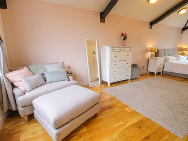 A bedroom with a bed lamps bedside tables chest of drawers a sofa and an ottoman at Timberdyne Brimfield near Woofferton