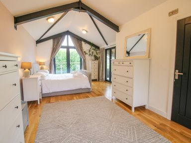 A bedroom with a bed lamps dressers a mirror and large windows at Timberdyne in Brimfield near Woofferton