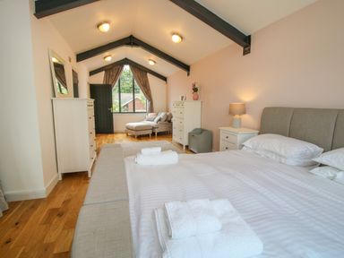 A bedroom with a double bed folded white towels two white dressers a chair near window with curtains at Timberdyne Brimfield near Woofferton