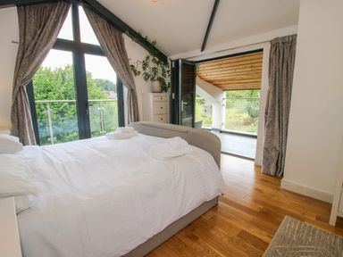 A bedroom with a double bed towels on bed wooden flooring and balcony doors at Timberdyne in Brimfield near Woofferton