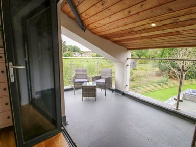 A balcony with two chairs and a small table overlooking a grassy yard at Timberdyne in Brimfield near Woofferton