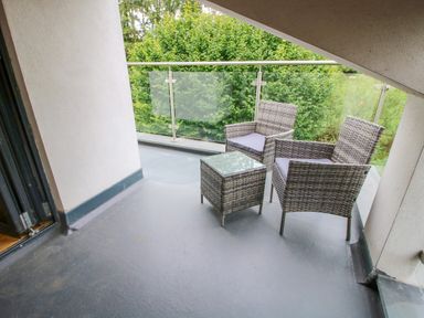 A balcony with two wicker chairs and a glass top table with trees in the background at Timberdyne in Brimfield near Woofferton