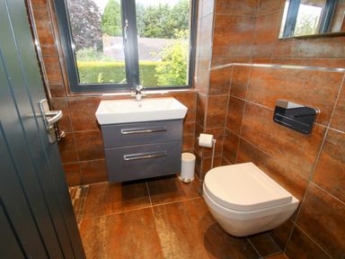 A bathroom with a wall-mounted sink cabinet a wall-mounted toilet and a window showing greenery outside at Timberdyne Brimfield near Woofferton