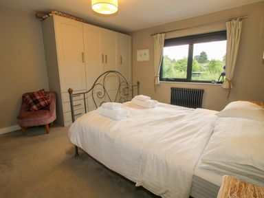 A bedroom with a metal bed frame white bedding towels on the bed white wardrobes a pink armchair and a window showing greenery outside at Timberdyne Brimfield near Woofferton