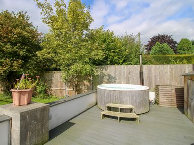A garden area with a round wooden hot tub and wooden steps surrounded by trees and wooden fencing at Timberdyne in Brimfield near Woofferton