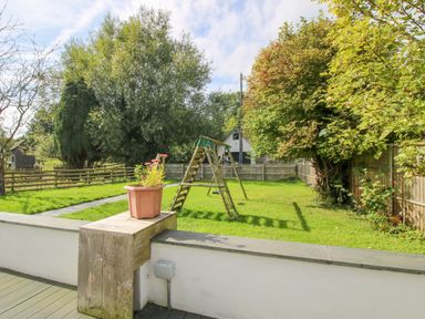 A garden with a swing set trees a flower pot on a wall and a wooden fence at Timberdyne Brimfield near Woofferton