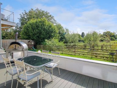 An outdoor patio with a glass table and four chairs next to a pizza oven and a fenced garden area at Timberdyne in Brimfield near Woofferton