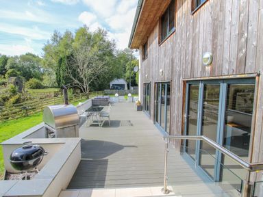 An outdoor patio with a grill table chairs and a wood paneled house at Timberdyne in Brimfield near Woofferton