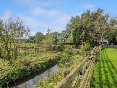 A small stream bordered by a wooden fence with hanging lights near green grassy land and trees at Timberdyne Brimfield near Woofferton