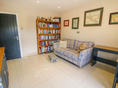 A room with a blue plaid sofa a wooden bookshelf filled with books framed maps on the wall and light tiled floor at Timberdyne Brimfield near Woofferton