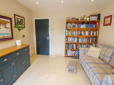 A room with a blue cabinet with a plant on top a black door a wooden bookshelf full of books a plaid sofa with cushions and a small footstool at Timberdyne Brimfield near Woofferton