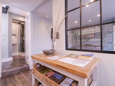 Interior view of a room with wooden table holding brochures and decorative bowl near a glass partition and an open door showing a bathroom with shower at Number 1 in Clare