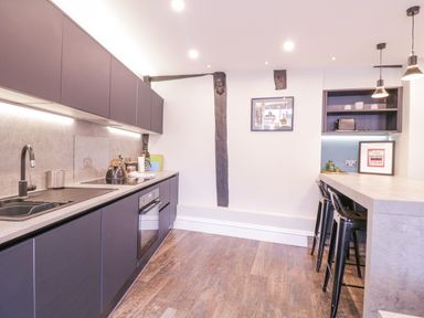A kitchen with dark cabinets, a countertop, stools at an island, and wooden floor at Number 1 in Clare