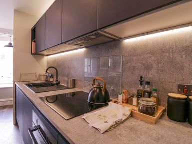A kitchen countertop with a black kettle, various jars and bottles on a wooden tray, a sink with a black faucet, and dark cabinetry above and below at Number 1 in Clare