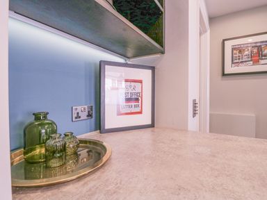 A countertop with green glass bottles on a brass tray and framed pictures on the wall at Number 1 in Clare