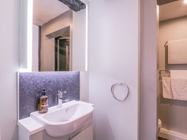 A bathroom sink with a faucet and soap dispenser under a lighted mirror and a towel ring on the wall at Number 1 in Clare