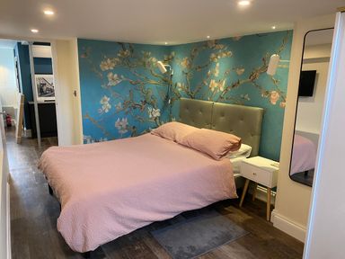 A bedroom with a double bed pink bedding floral wallpaper wooden floor and a bedside table at Number 1 in Clare