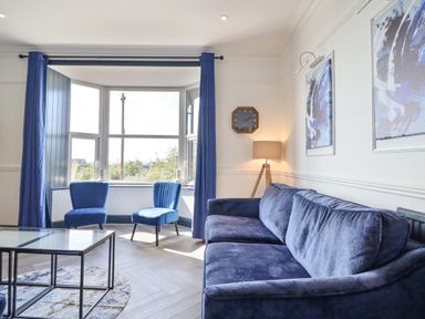 A living room with blue velvet sofa and chairs with floor lamp and wall clock at Gwynfa in Barmouth