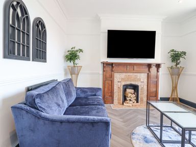A living room with a blue sofa a fireplace a wall mounted tv two plants and a glass coffee table at Gwynfa in Barmouth
