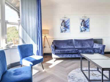 A living room with blue sofa and chairs a glass coffee table and two abstract paintings at Gwynfa in Barmouth